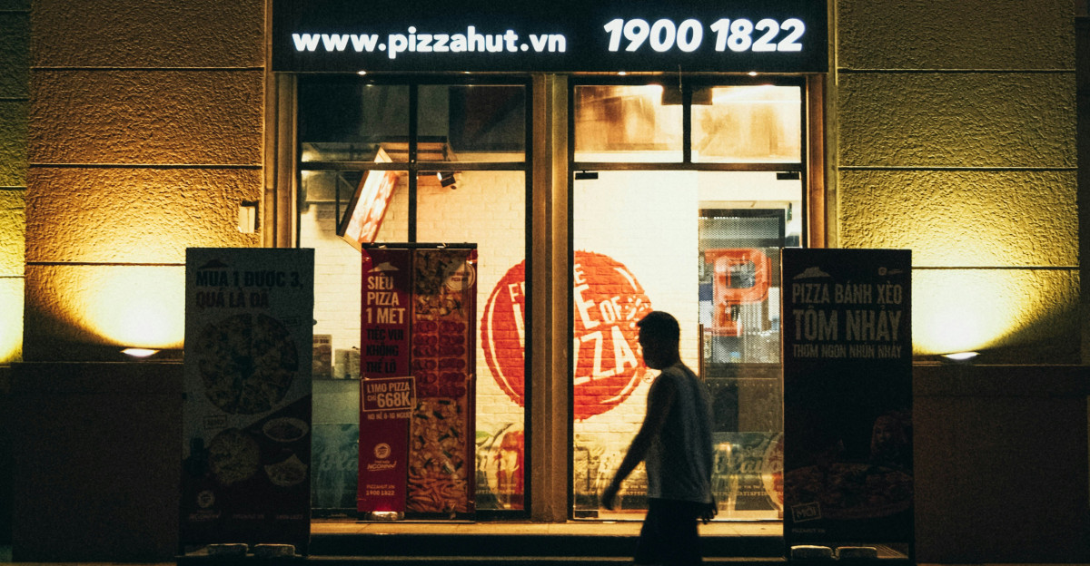 a man walking past a pizza hut at night