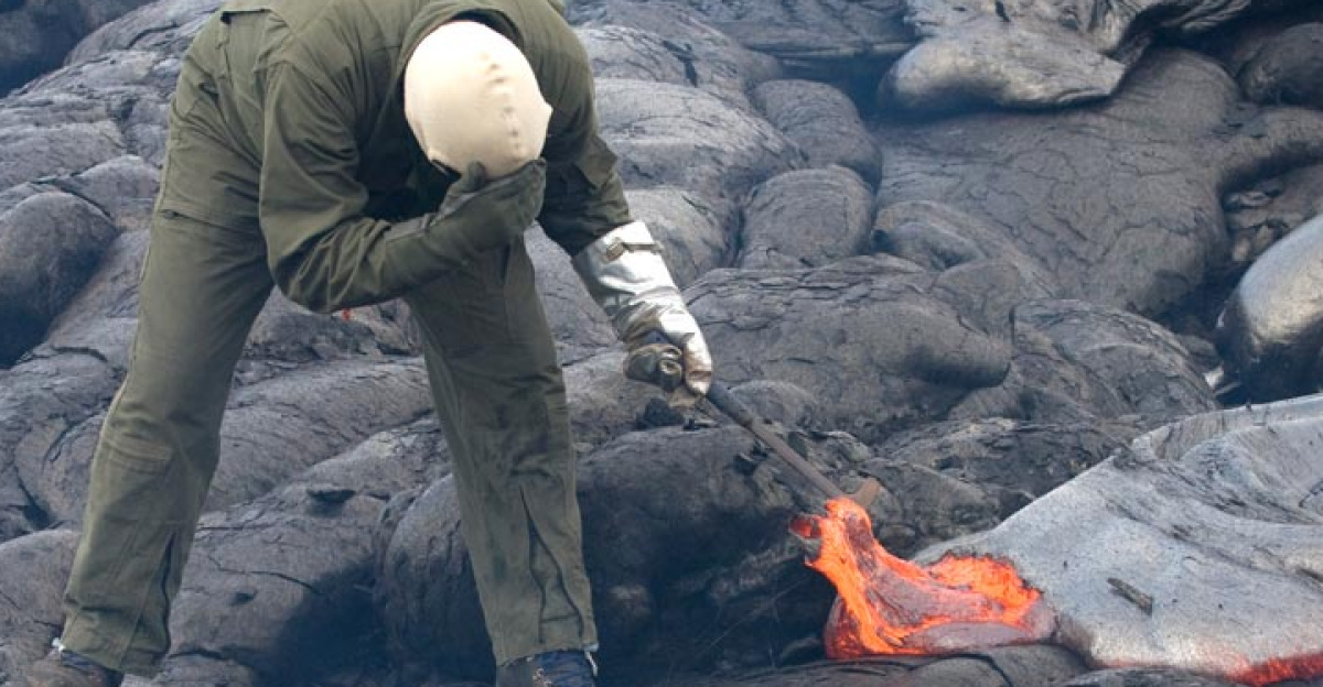 A geologist collecting a lava sample for chemical analyses from an active lava flow on Kilauea, using a rock hammer and a bucket of water.