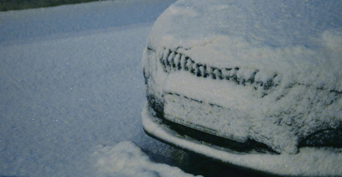 A car buried under snow during a winter snowfall, creating a serene and cold atmosphere.