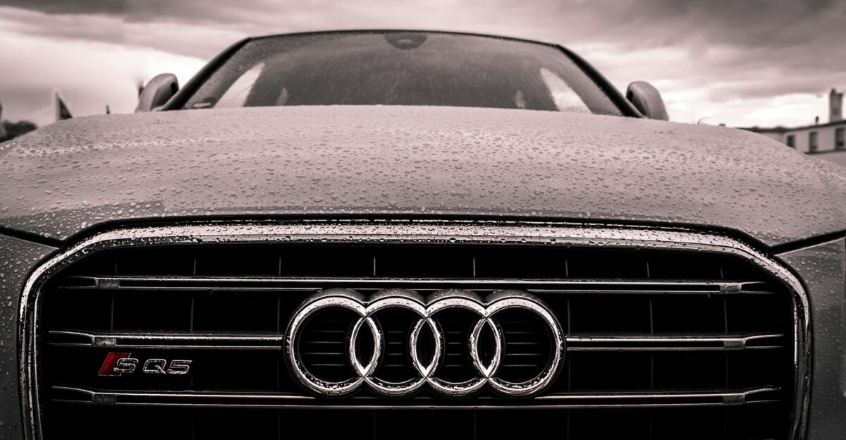 Close-up of a rain-covered Audi car grille showcasing luxury and elegance under cloudy skies