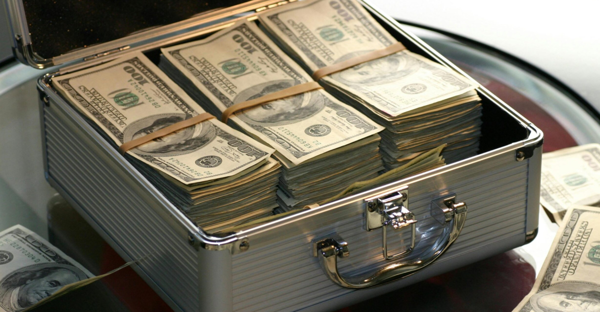 Open briefcase filled with stacks of hundred dollar bills on a glass table, representing wealth.