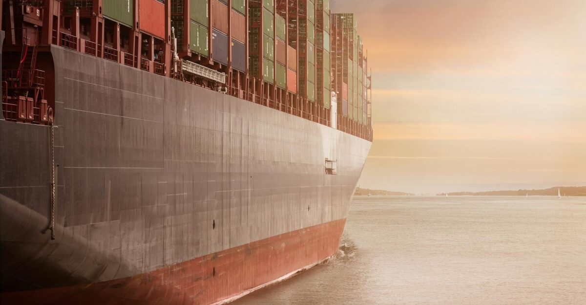 A colossal cargo ship loaded with containers navigates through calm waters against a vibrant sunset sky