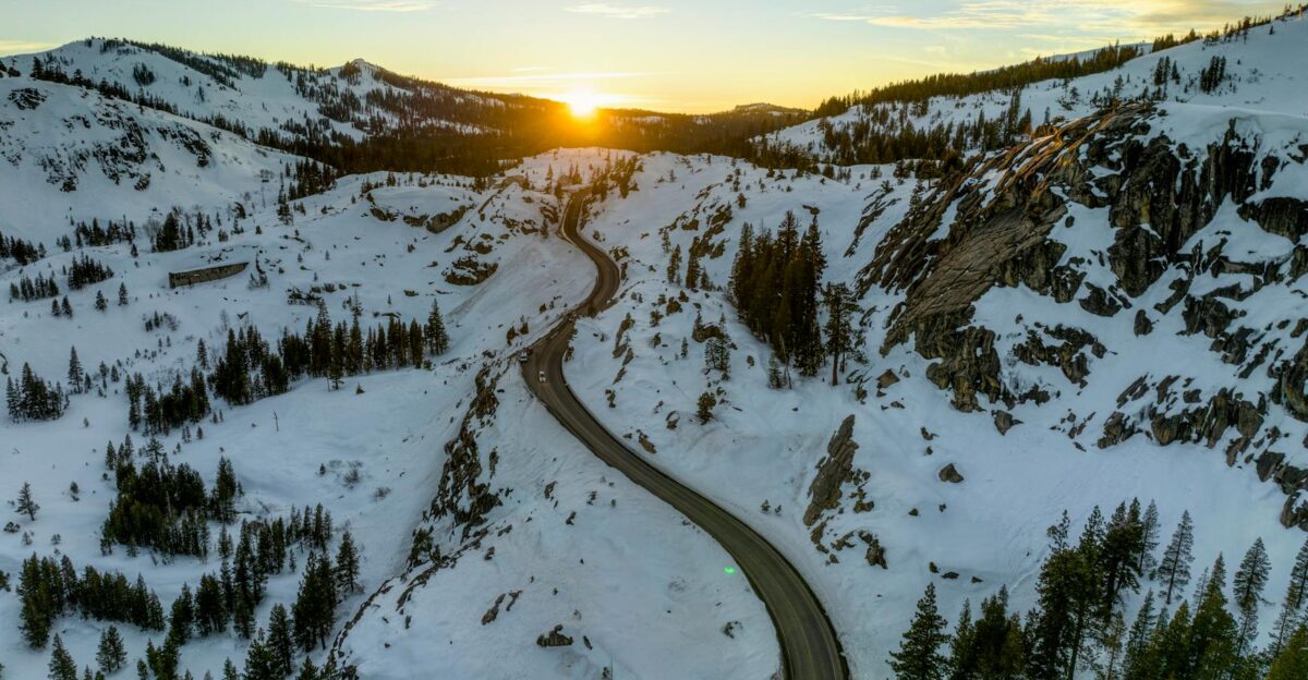 A mesmerizing aerial view of a snowy Sierra mountains landscape at sunset showcasing a winding road amidst winter wilderness