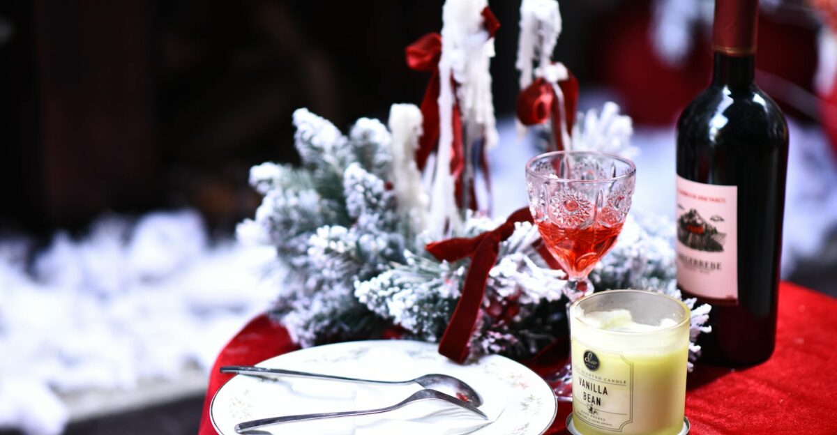 Cozy winter dinner setting featuring wine candle and snowy decor on a red tablecloth