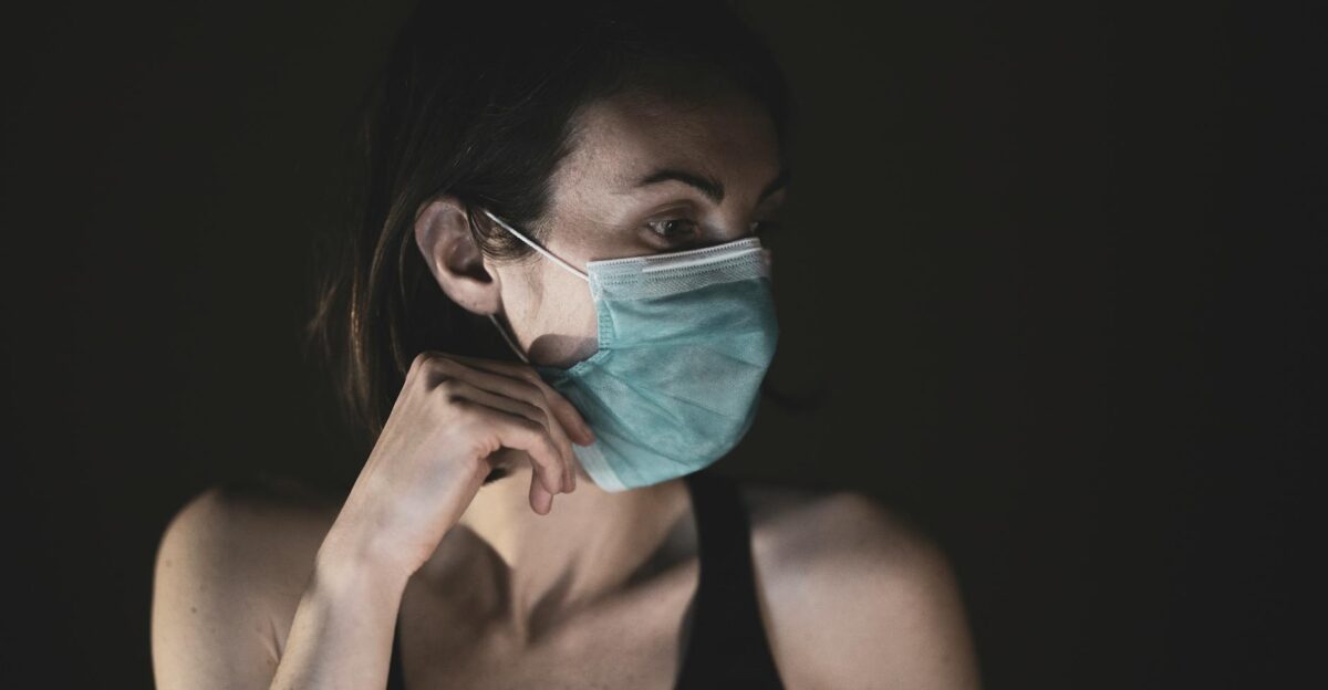 A contemplative woman wearing a face mask in low-light conditions symbolizing pandemic awareness