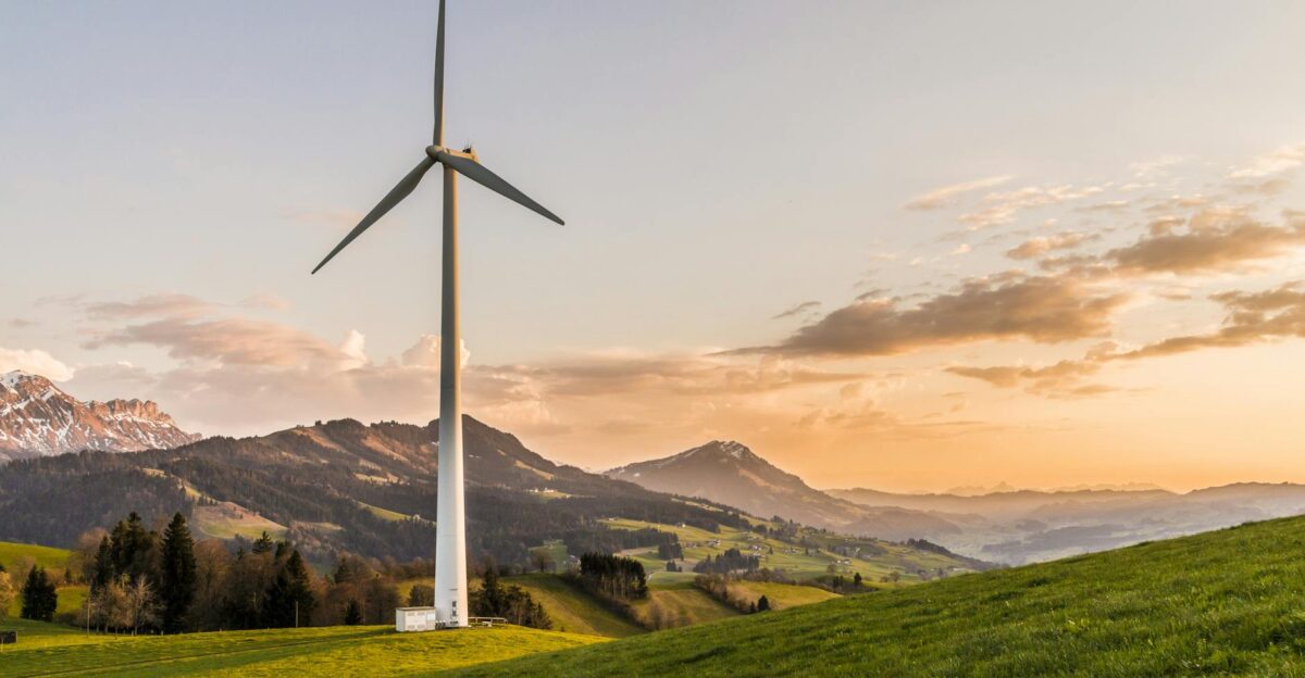Wind turbine amid rolling hills and mountains at sunset symbolizing renewable energy and sustainability