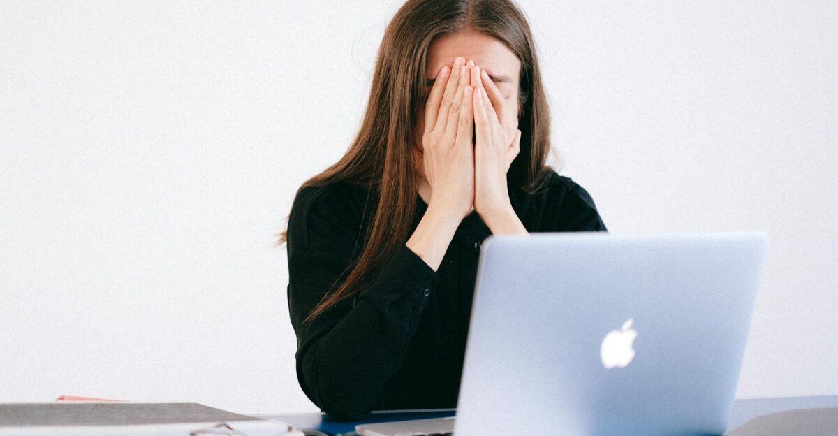 Woman feeling stressed and overwhelmed at her desk while working remotely on a laptop