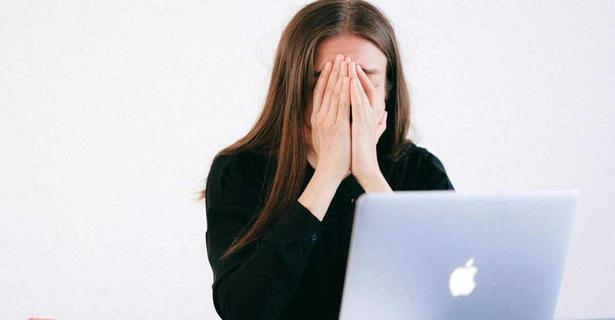 Woman feeling stressed and overwhelmed at her desk while working remotely on a laptop.