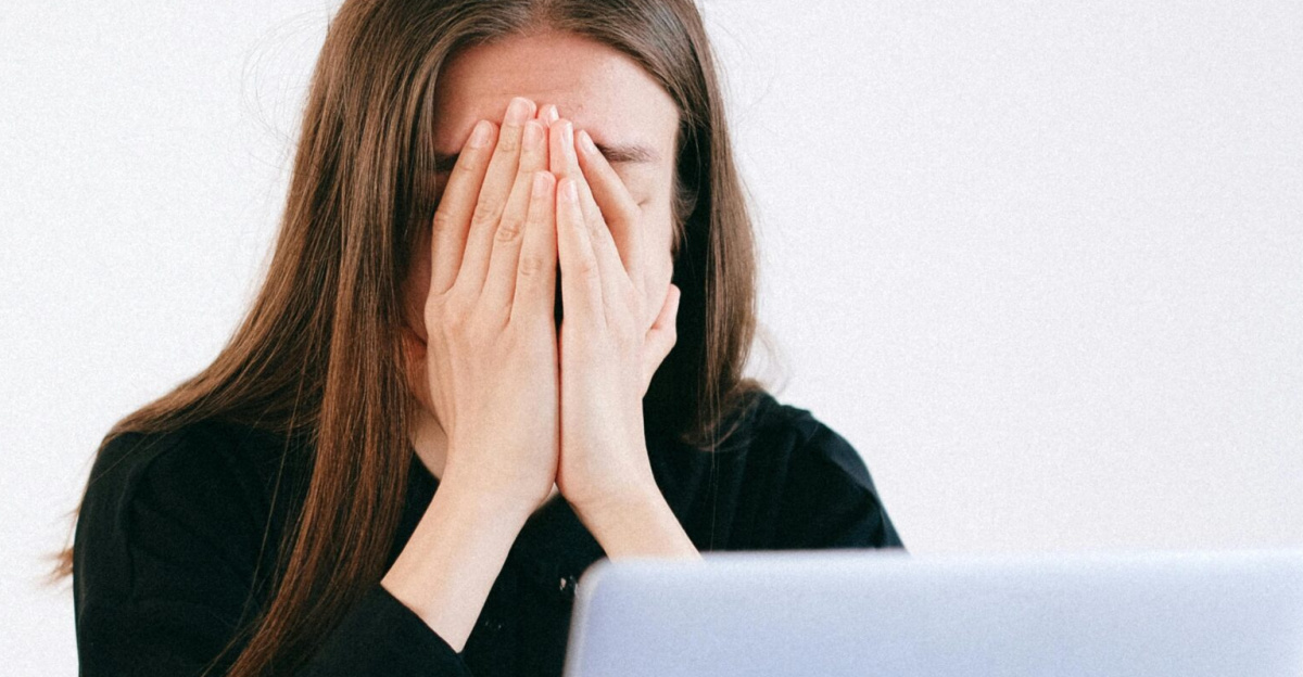 Woman feeling stressed and overwhelmed at her desk while working remotely on a laptop.