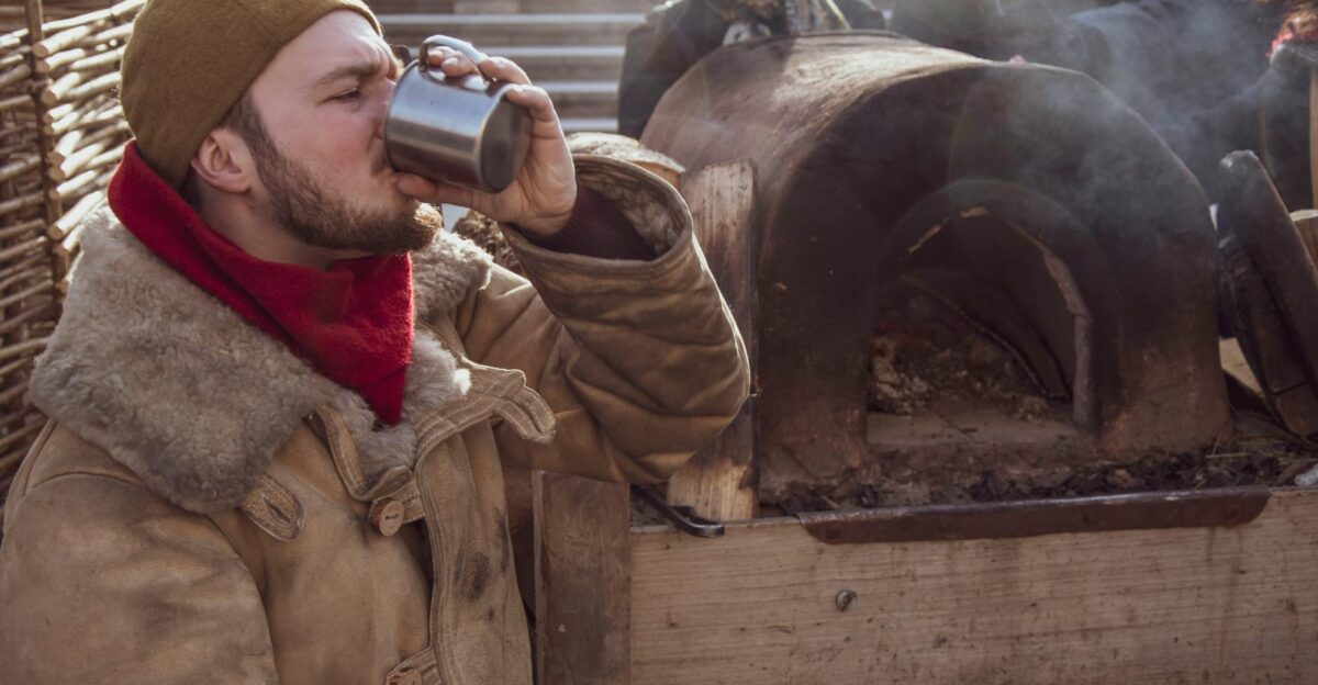 Man enjoys a drink by a traditional Russian oven at a winter festival in Moscow