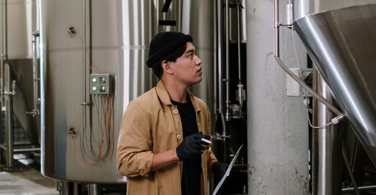 Asian man inspecting stainless steel tanks in a brewery, showcasing modern industrial processes.
