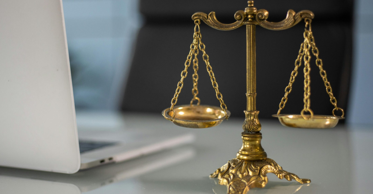 Golden justice scales on a desk beside a laptop, symbolizing law and balance.