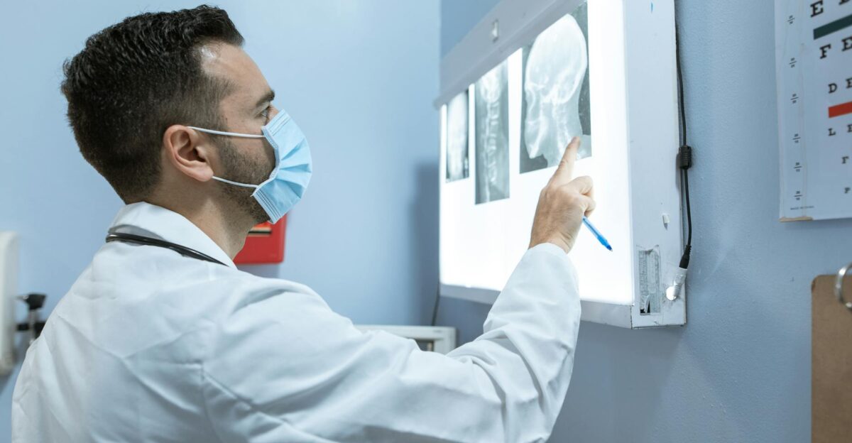 A healthcare professional examines brain X-rays while wearing a face mask in a hospital setting