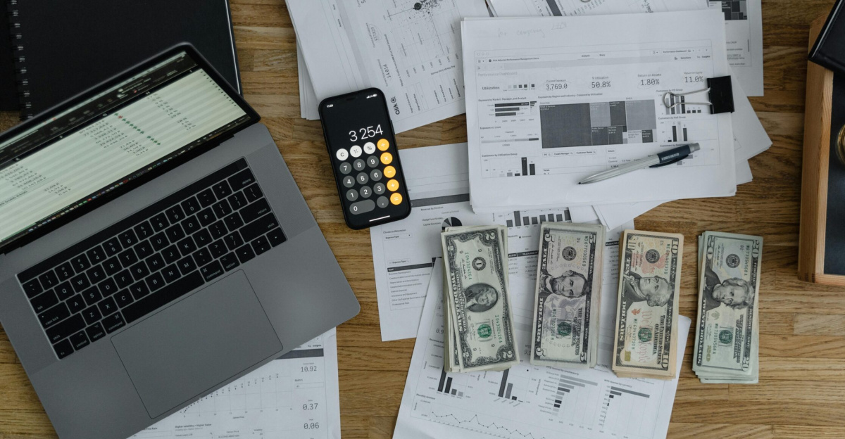 Overhead view of financial documents, cash, and technology on a wooden desk.