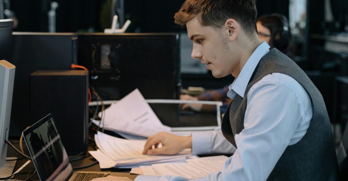 Young male professional focused on work with laptop and documents at office desk