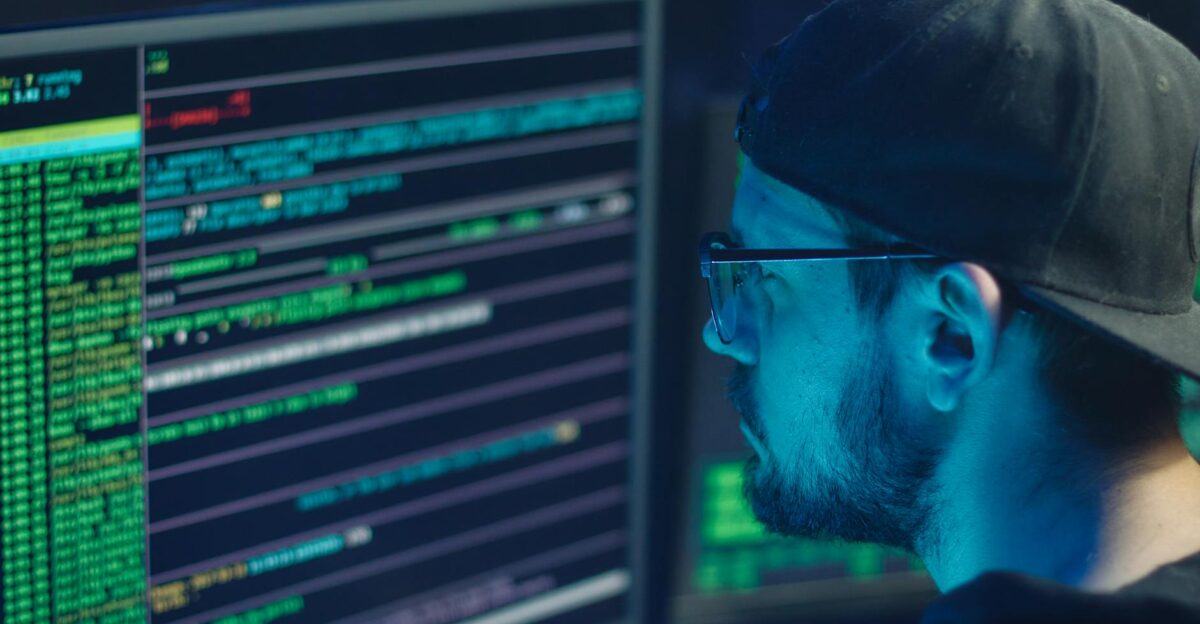 A cybersecurity expert inspecting lines of code on multiple monitors in a dimly lit office