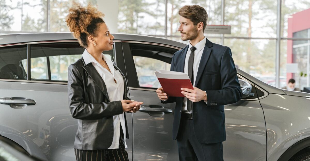 A woman discussing car purchase with a dealer inside a car dealership showroom