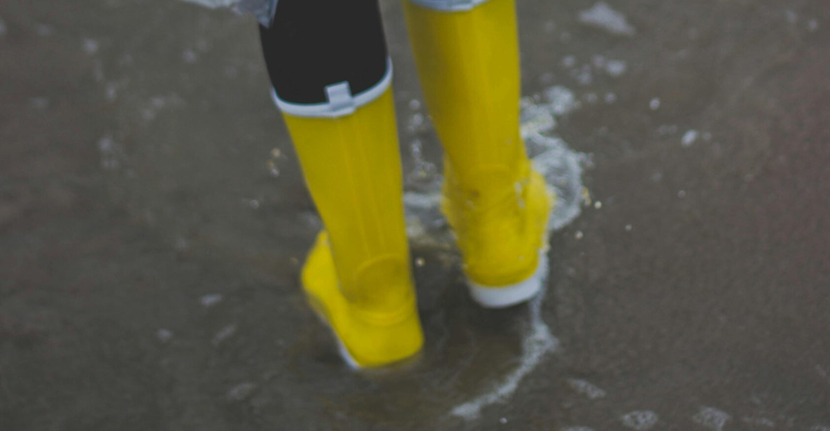 Person wearing yellow boots and raincoat, splashing through water outdoors.