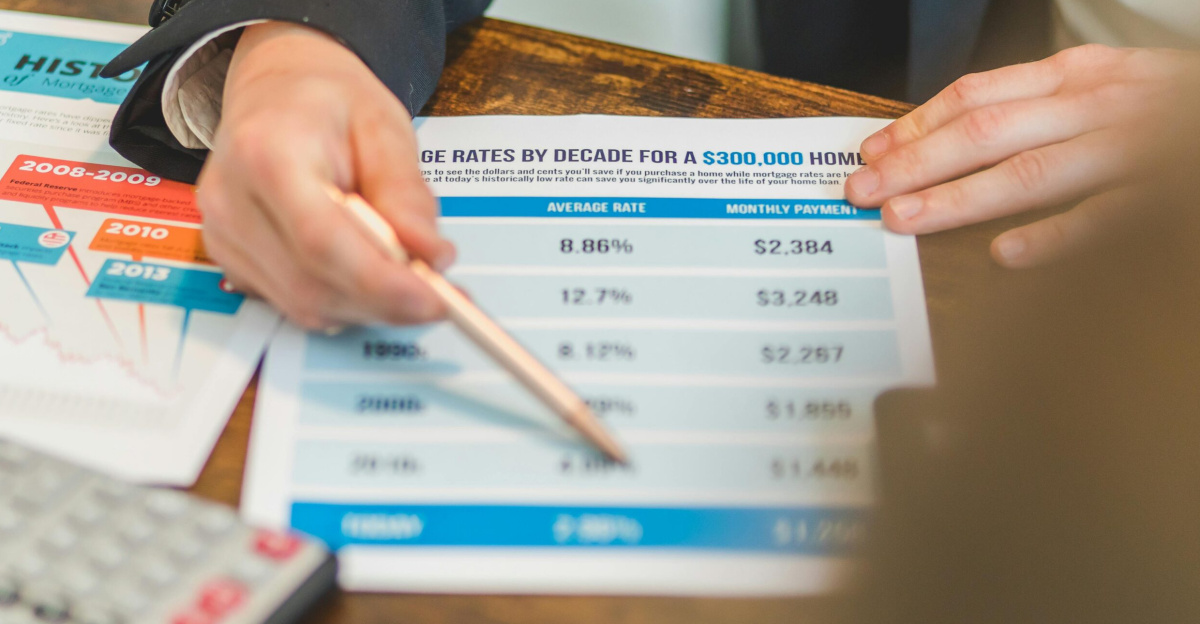 A close-up of hands analyzing mortgage rate documents with a pen and calculator in a business setting.