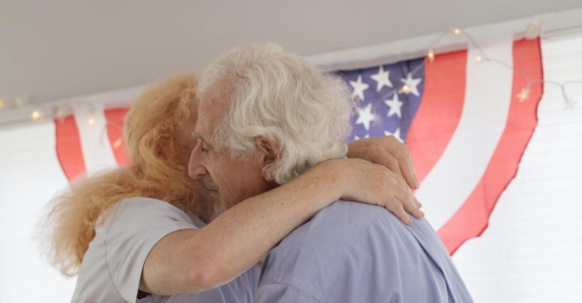 Senior couple embracing with American flag backdrop celebrating togetherness and freedom