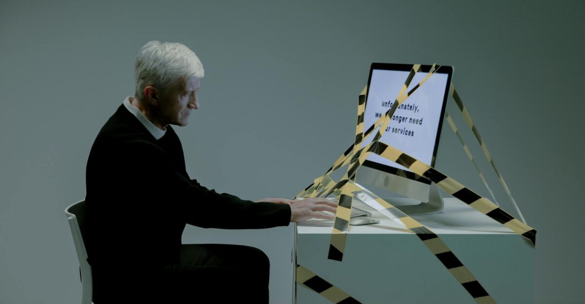 An elderly man sits at a desk with a computer dealing with job termination notice