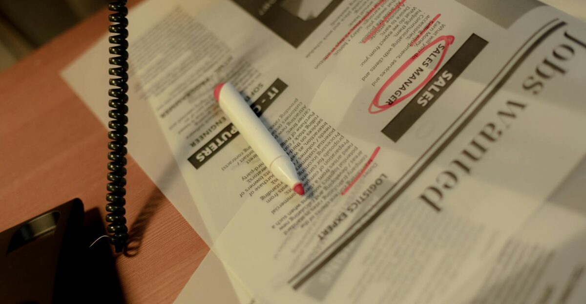Close-up of a newspaper job section with a red marker and corded phone on a table