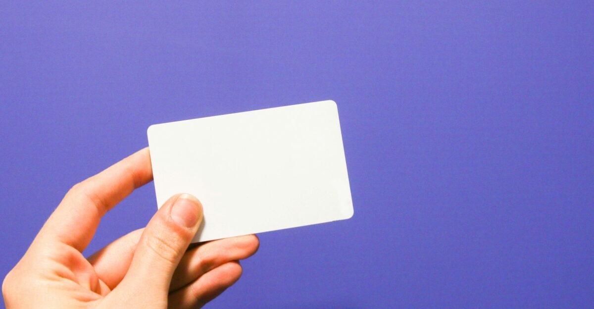 a hand holding a white business card against a purple background
