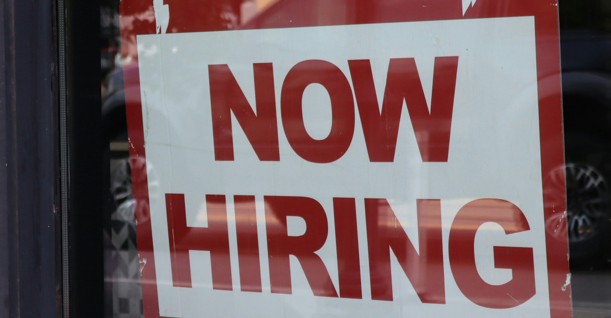 A "now hiring" sign hangs in a store window.