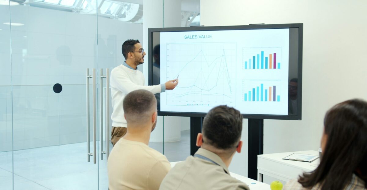 Man presenting charts on a large screen to audience